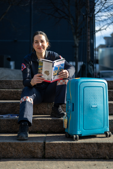 Kvinne i uniform sitter med koffert og leser guidebok.