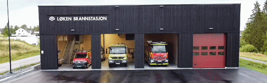 Brunt, firkantet bygg med fire porter og tre er åpne og viser ulike typer brannbiler.